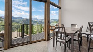 A dining area with a table and chairs, large sliding glass doors, and a view of mountains. - Aspen Trail Retreat - Breathtaking Mountain Views! (Estes Park)