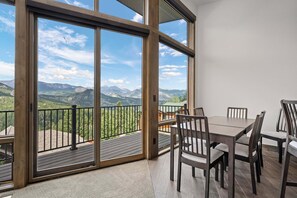 A dining area with a table and chairs, large sliding glass doors, and a view of mountains. - Aspen Trail Retreat - Breathtaking Mountain Views! (Estes Park)