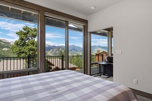 Quarto com uma grande janela, colcha xadrez e vista para as montanhas.
