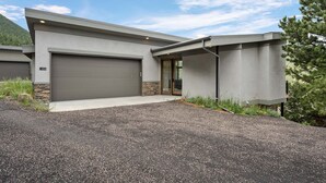 A modern two-story house with a garage, a stone foundation, and a gravel driveway. - Aspen Trail Retreat - Breathtaking Mountain Views! (Estes Park)