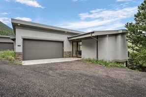 A modern two-story house with a garage, a stone foundation, and a gravel driveway. - Aspen Trail Retreat - Breathtaking Mountain Views! (Estes Park)
