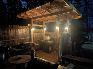 Une terrasse extérieure en bois, équipée d’un barbecue, d’une table et d’un banc.