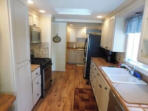 A kitchen with white cabinetry, a black refrigerator, and a wooden floor.