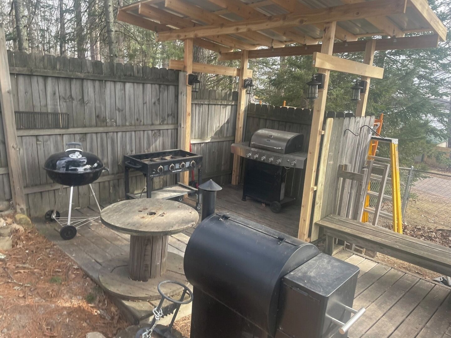 An outdoor patio with a wooden pergola, a grill, a round table, and a barbecue smoker.