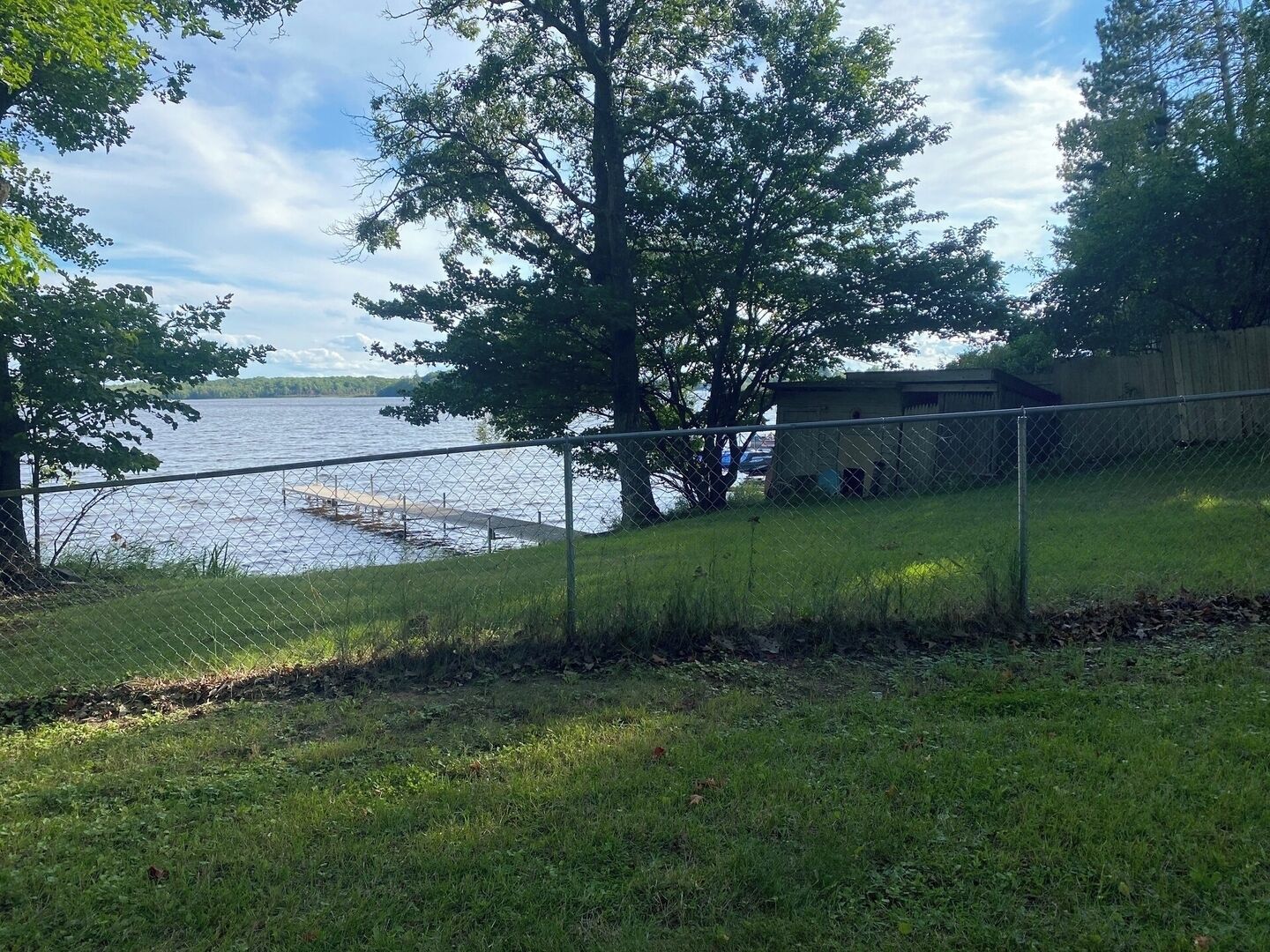 A fenced outdoor area with a dock extending into a body of water, surrounded by trees and a grassy area.