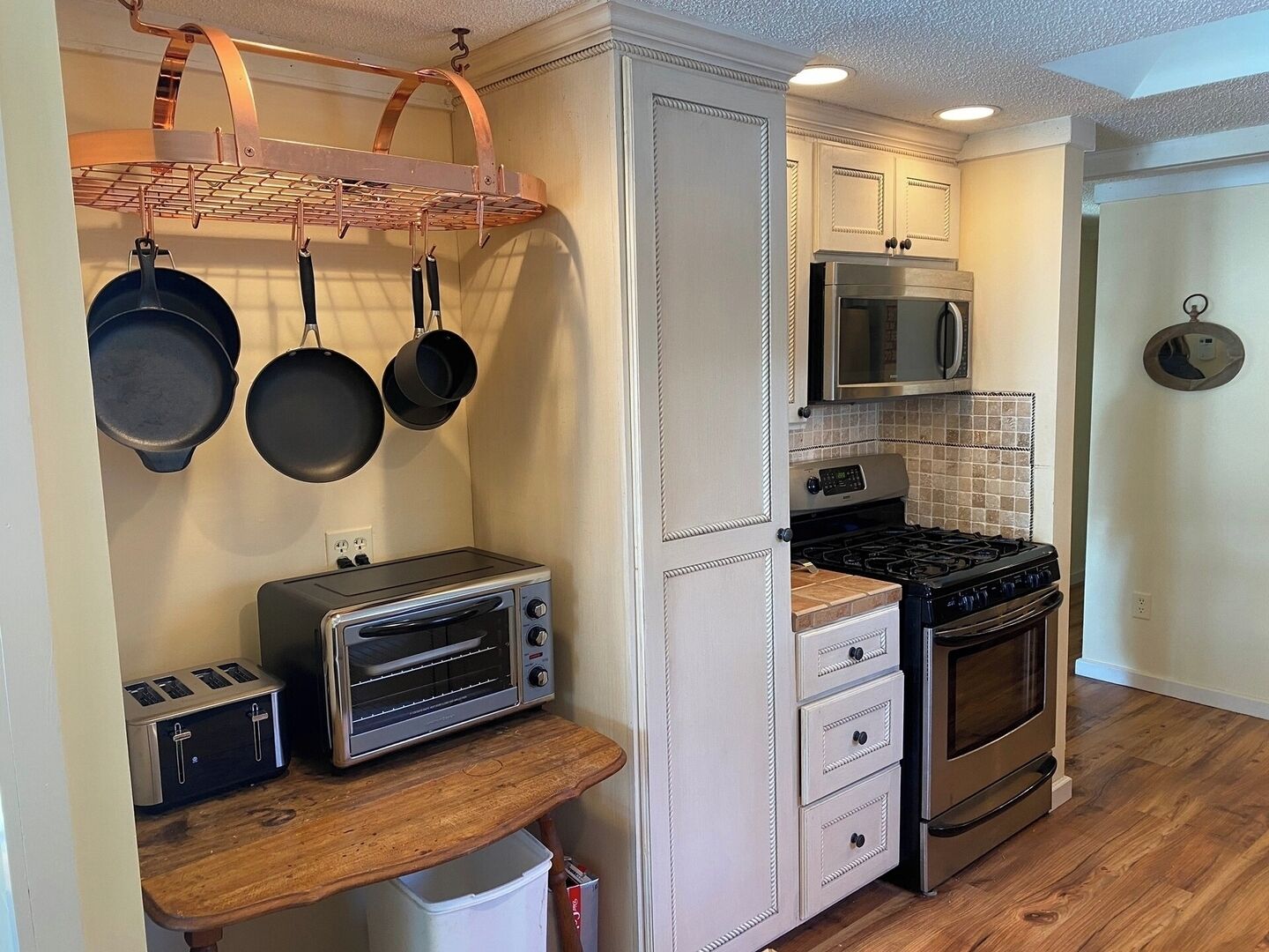 A compact kitchen with a toaster, oven, microwave, and hanging cookware.