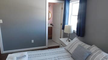 A bedroom with a bed, a nightstand, a lamp, and a view of a bathroom.