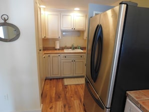 A kitchen with wooden flooring, a stainless steel refrigerator, and white cabinetry.