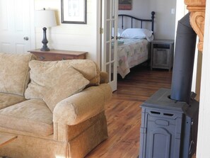 A room with a sofa, a bed with a quilt, a lamp, and a wood-burning stove.