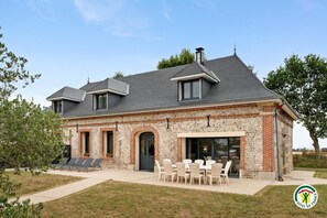 Ein zweistöckiges Haus mit Ziegelaußenwand, geneigtem Dach und einer Terrasse mit Sitzgelegenheiten.