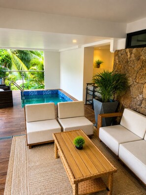A modern living room with a pool, white sofas, a wooden coffee table, and a stone accent wall.
