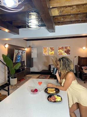 Eine Person sitzt an einem Tisch mit Essen und einem Getränk in einem Raum mit Holzbalken, einem Fernseher und Kunstwerken an der Wand.