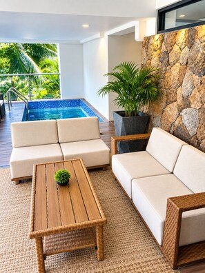 A modern indoor pool area with a stone wall, a sofa, a coffee table, and a potted plant.