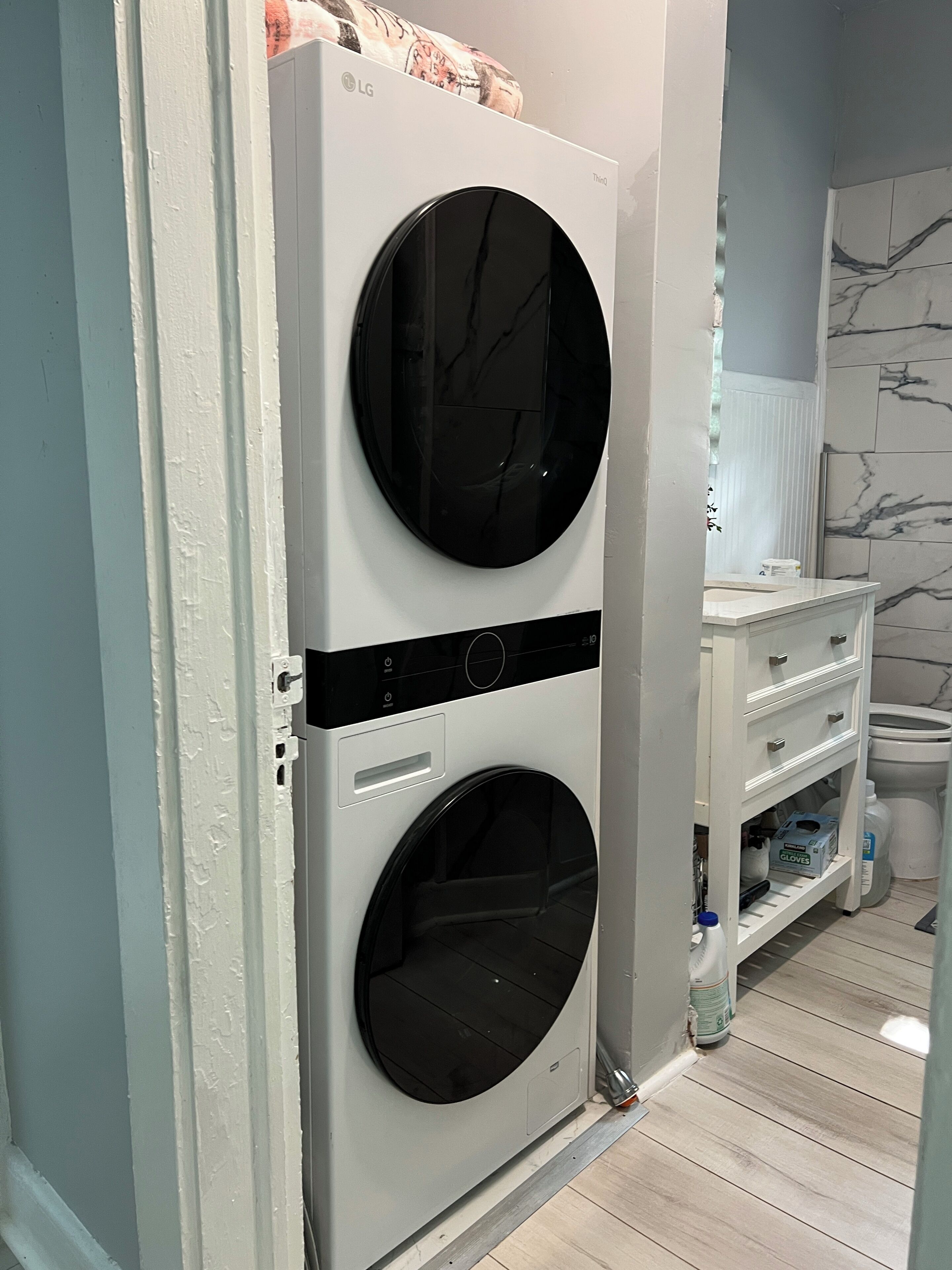 A laundry room with two stacked washing machines, a white cabinet with drawers, and a marble-patterned wall.