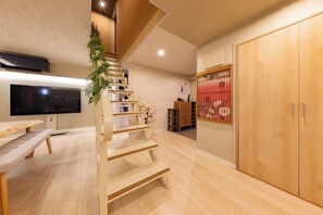 A modern interior with a wooden staircase, a flat-screen TV, a dining table, and a traditional sliding door. - Central Namba and Dotonbori | Spacious 7-bedroom, 1-living room, 1-dining room, 1-kitchen unit with a panoramic open-air bath and BBQ, accommodating up to 14 guests (大阪市)