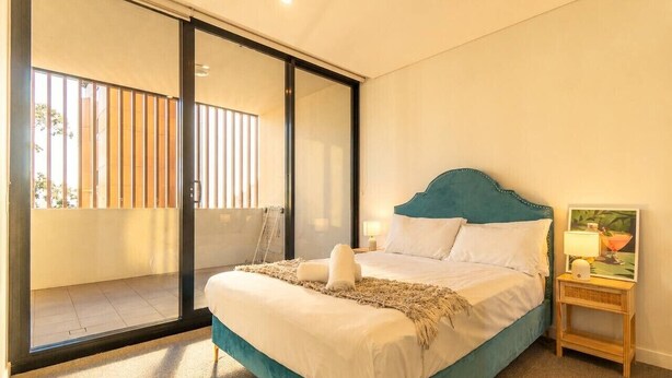 Un dormitorio con cama, mesita de noche, lámpara y vista a un balcón.
