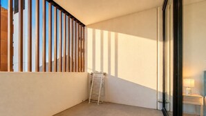 Habitación de esquina con suelo de baldosas, un perchero metálico y una puerta de cristal que da a otra habitación.