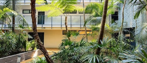 A courtyard with a wooden deck, palm trees, and a building with a balcony.