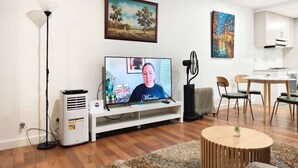A living room with a flat-screen TV, a white entertainment unit, a standing fan, and a dining area with chairs and a table. - Dee Why 2BR Apartment Near Beach & Shops (Dee Why)
