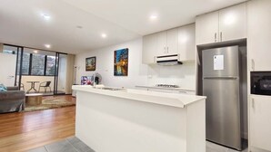 A modern kitchen with a central island, stainless steel appliances, and a dining area with a view. - Dee Why 2BR Apartment Near Beach & Shops (Dee Why)