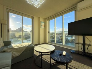 Ein modernes Hotelzimmer mit großem Fenster, einer Couch, einem runden Tisch und einem Flachbildfernseher.