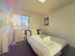 Ein Hotelzimmer mit Bett, kleinem Tisch, Stuhl, Heizkörper und Fenster mit Blick auf die Stadt.