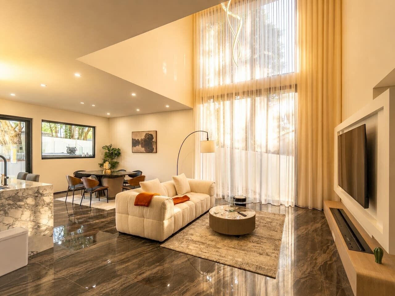 A modern living room with a sofa, coffee table, and TV. There is a dining area with chairs and a table.