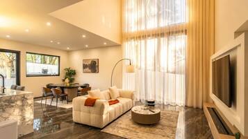 A modern living room with a sofa, coffee table, and TV. There is a dining area with chairs and a table.
