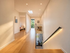 A modern interior with a wooden floor, a staircase with a glass railing, and a view of greenery outside.