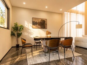 A modern dining area with a round table, four chairs, a potted plant, and a painting on the wall.