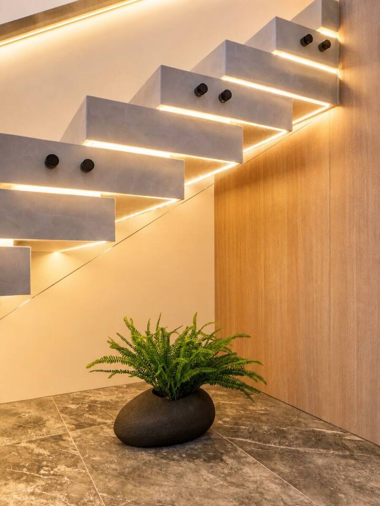 A modern staircase with integrated lighting, a potted plant, and a wooden wall.