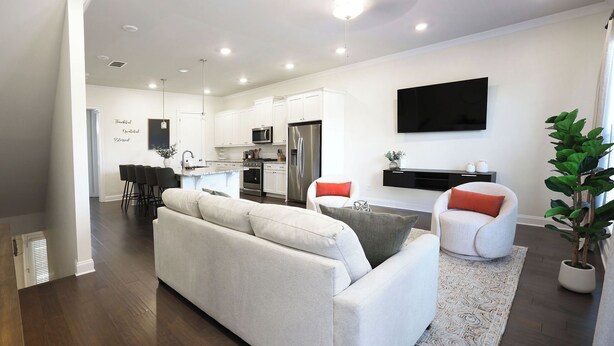 Una sala de estar moderna con un sofá, dos sillones, un televisor de pantalla plana y una cocina al fondo.