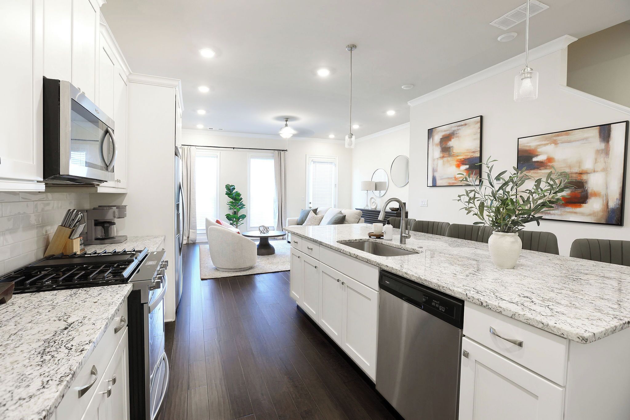 A modern kitchen with white cabinetry, a granite countertop, a built-in dishwasher, and a dining area with a sofa and table.
