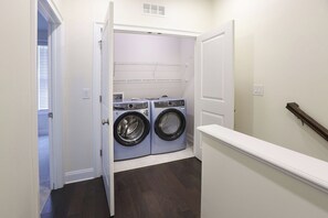 A laundry room with two front-loading washing machines and a dryer, a white door, and a wooden handrail. - Stylish 3BR/3BA Atlanta Retreat. Quiet Neighborhood, Close to Stadiums & Dining (Atlanta)