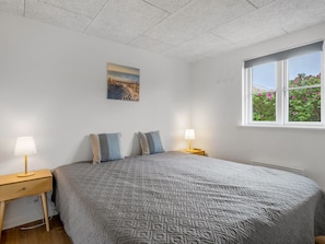 Ein Schlafzimmer mit einem Bett, zwei Nachttischen mit Lampen, einem Fenster mit Blick ins Grüne und einem Gemälde an der Wand.