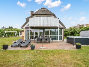 A modern house with a curved roof, large glass windows, a patio with outdoor furniture, and a garden. - "Algut" - 200m from the sea by Interhome (Blåvand)