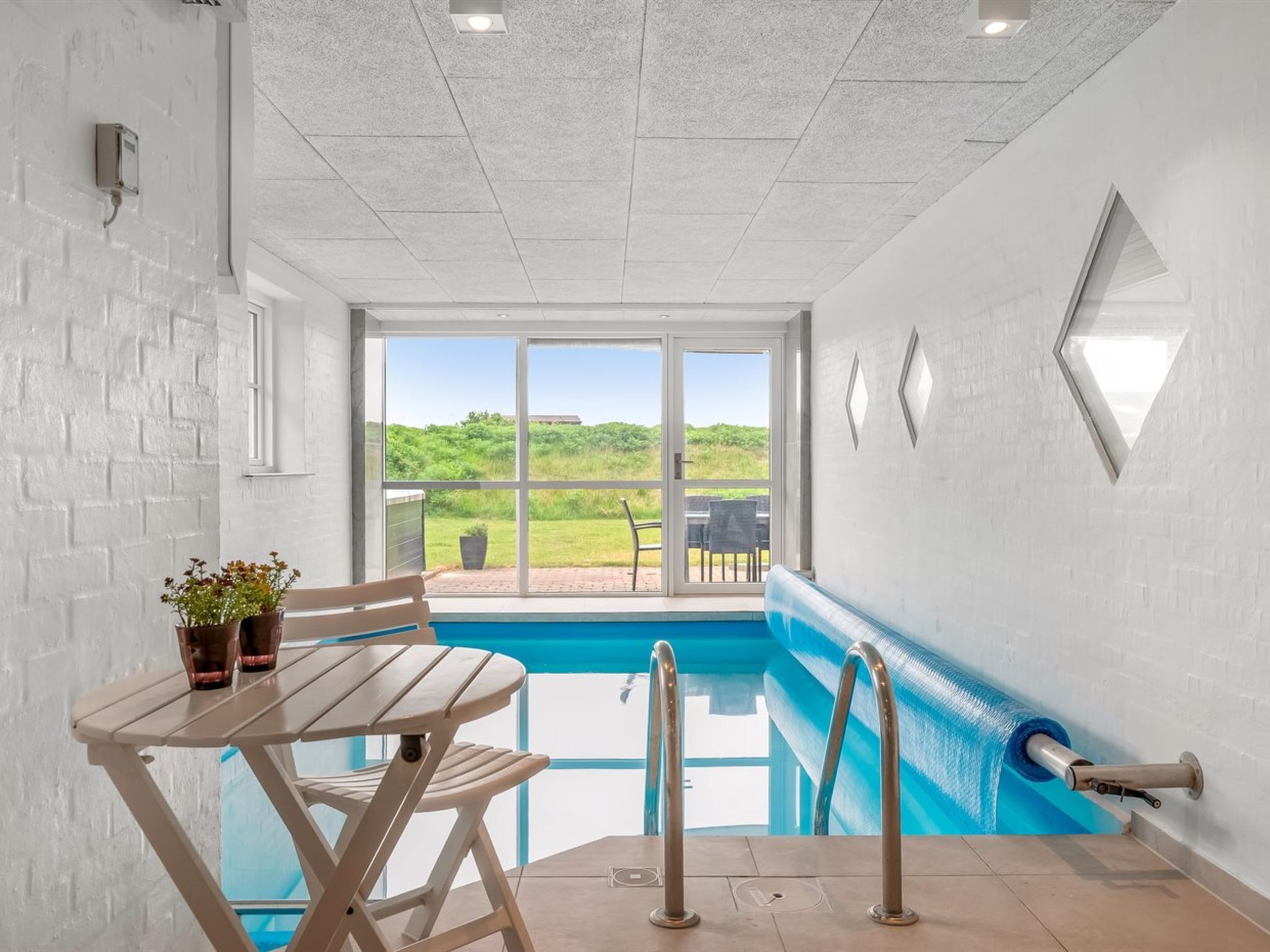 Un espace piscine avec une table et des chaises, une vue sur l’extérieur et un ciel dégagé.