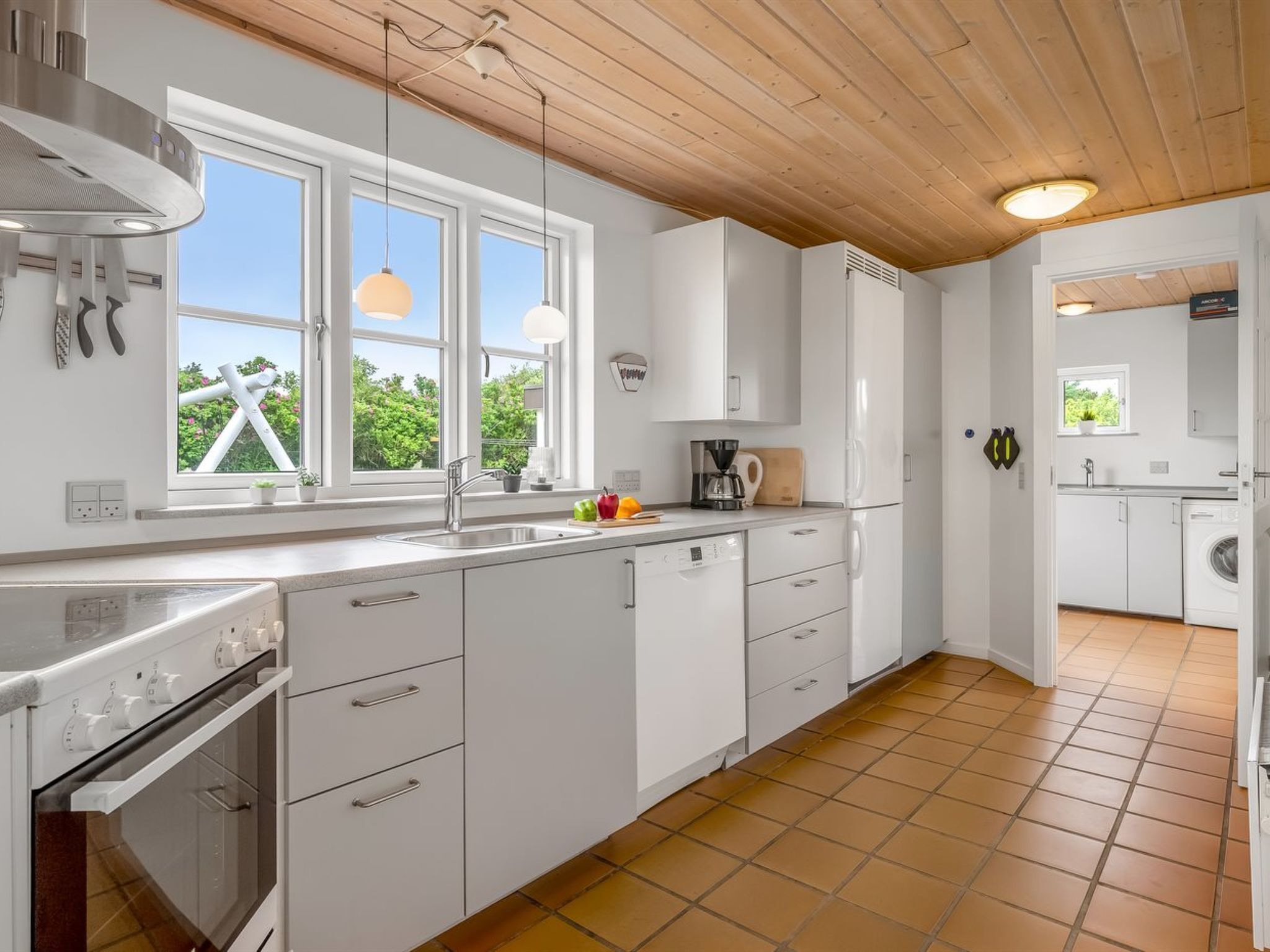 Une cuisine moderne avec des meubles blancs, un four encastré et une fenêtre donnant sur un espace verdoyant.