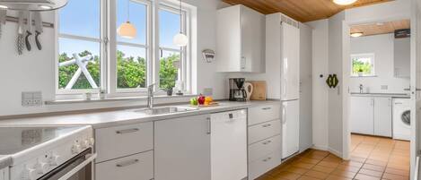 Una cucina moderna con mobili bianchi, forno integrato e finestra con vista sul verde.