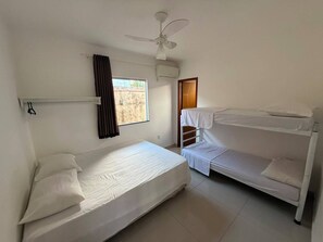 Une chambre avec un lit simple, un lit superposé, un ventilateur de plafond et une fenêtre avec des rideaux.