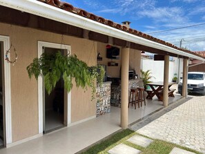 A covered outdoor area with a barbecue setup, a seating arrangement, and a vehicle parked nearby. - Recanto do Benji - Piscina e Sauna- Proximo a praia (Santa Cruz Cabrália)