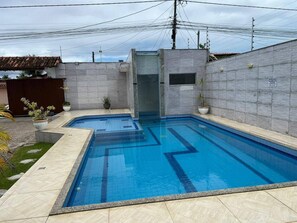 Ein rechteckiger Swimmingpool mit klarem, blauem Wasser, umgeben von einer gefliesten Liegefläche und einer niedrigen Steinmauer.