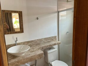 Een badkamer met een wit wastafelmeubel, een spiegel met decoratieve lijst, een toilet en een douchecabine met glazen wanden.