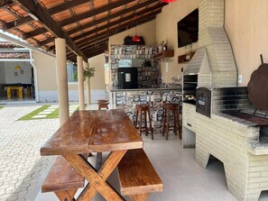 Une terrasse extérieure avec une table et des bancs en bois, un four en briques et un coin bar agrémenté d’un mur recouvert de carreaux.