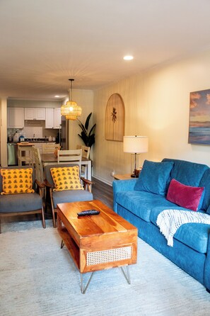 A living room with a blue sofa, a wooden coffee table, and a dining area in the background. - Coastal Oasis Near Coligny Beach (Hilton Head Island)