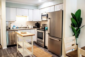 A modern kitchen with stainless steel appliances, white cabinetry, and a wooden table. - Coastal Oasis Near Coligny Beach (Hilton Head Island)