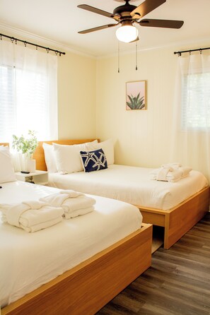 A hotel room with two beds, a ceiling fan, a bedside table with a lamp, and a window with curtains. - Coastal Oasis Near Coligny Beach (Hilton Head Island)