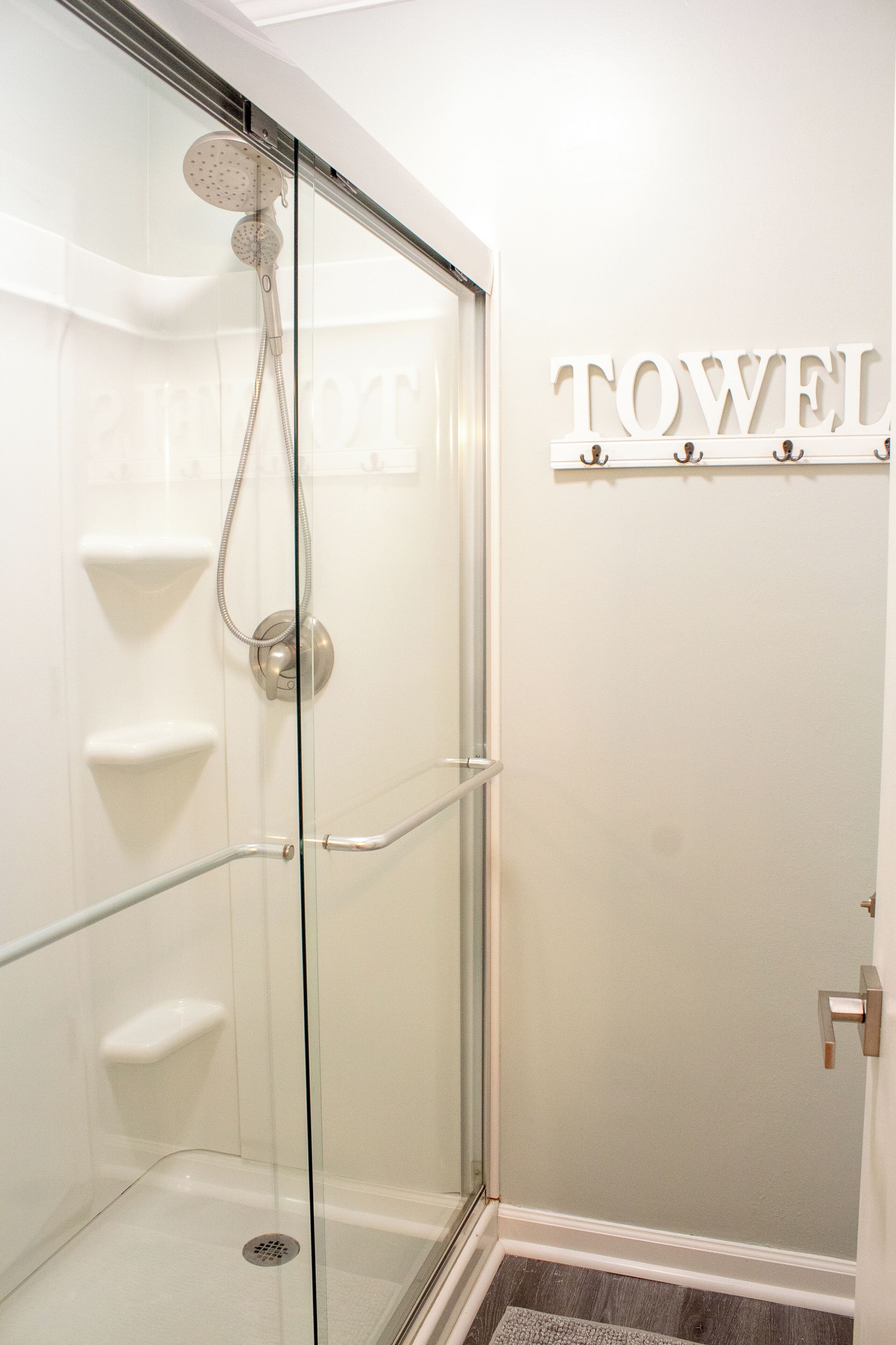 A glass-enclosed shower with a handheld showerhead and a towel rack with the word 'TOWEL' on the wall.