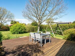 A wooden deck with a table and chairs, surrounded by greenery and a swing set. - "Aida" - 550m from the sea by Interhome (Esbjerg V)