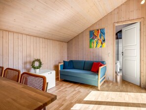A room with a wooden ceiling, a blue sofa with red cushions, a dining table with chairs, and a small white refrigerator. - "Aida" - 550m from the sea by Interhome (Esbjerg V)